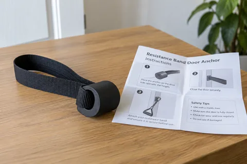 Purpose-made resistance band door anchor and its instruction leaflet laid on a table.