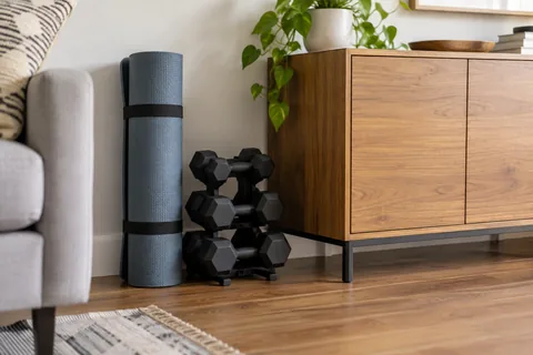 Rolled exercise mats and a compact dumbbell rack beside a living-room cabinet.