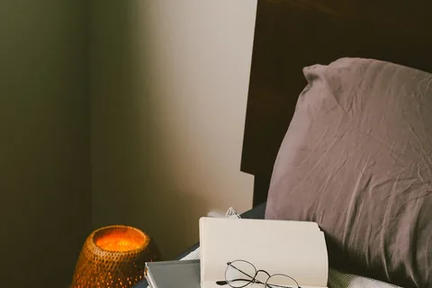 A softly lit bedside corner with a book and pillow.